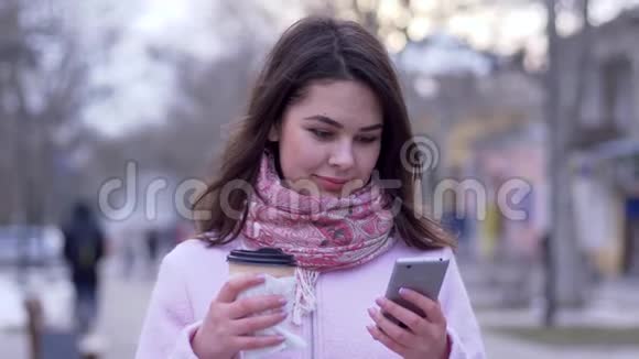 在网络交流中女士坐在社交网络中走路时手里拿着智能手机和一杯咖啡视频的预览图
