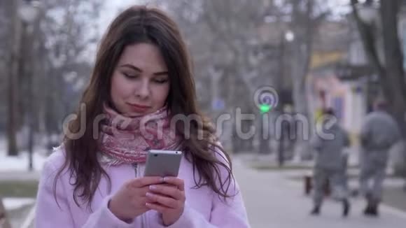 网络成瘾微笑的女孩手里拿着智能手机在露天特写镜头上行走视频的预览图