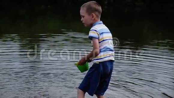 小男孩尖叫着怒气冲冲地从桶里的水倒进河里儿童自然游戏视频的预览图
