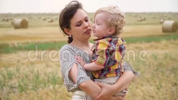 一位美丽的年轻女子她的怀里抱着一个金发小儿子在一片麦田里夏天带着包视频的预览图