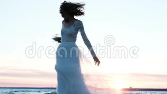 快乐的欧洲新娘穿着婚纱在海滩上日落时分一束原始的手工纺成的花朵视频的预览图