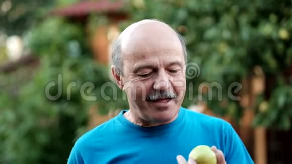 穿着蓝色t恤的白人老人在户外吃新鲜苹果农民品尝秋收视频的预览图