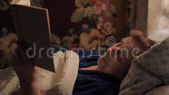 一位老妇人躺在毯子下面的床上看书视频的预览图
