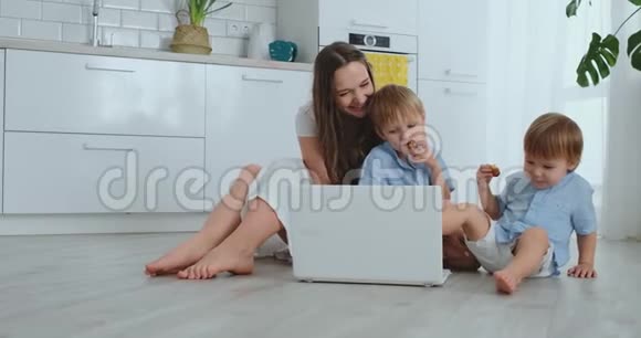 现代公寓爱妈妈和两个小儿子坐在客厅的地板上看着笔记本电脑屏幕视频的预览图