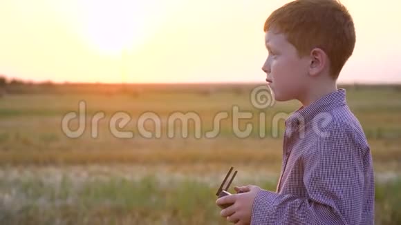傍晚日落时分红发男孩站在一片麦田上手里拿着捆控制着无人机视频的预览图