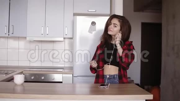 20多岁的小女孩在厨房里跳舞耳朵里戴着耳机从桌子上拿起一个杯子视频的预览图