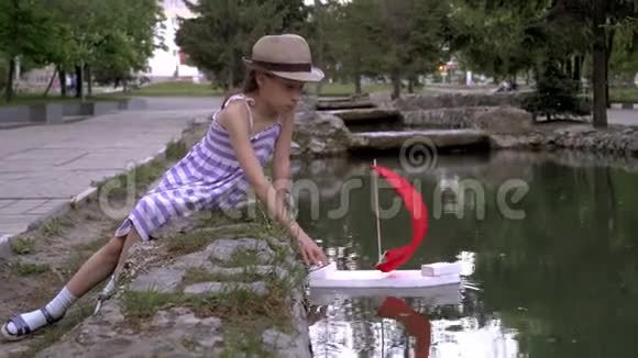 一个小女孩在公园的夏天在城市池塘里发射一艘带着红色帆的船红帆视频的预览图