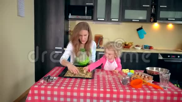可爱的小帮手女孩和美丽的母亲把饼干放进烤箱锡里视频的预览图