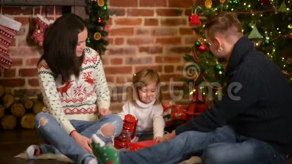 家人平安夜在壁炉家长和小孩子开启圣诞礼物带礼品盒的儿童生活起居视频的预览图