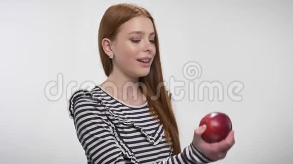年轻的姜姑娘正咬着红苹果享受着它白色的背景视频的预览图