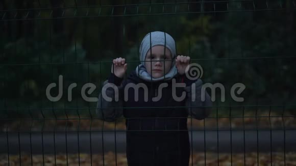 孤独的不快乐的可怜的小男孩在背后紧紧抓住篱笆视频的预览图