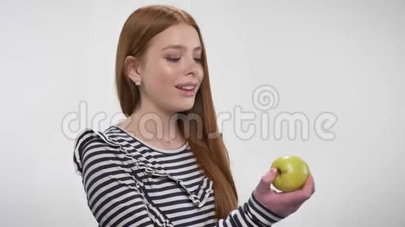 年轻的甜姜姑娘在咬苹果提供它交流理念白色背景视频的预览图