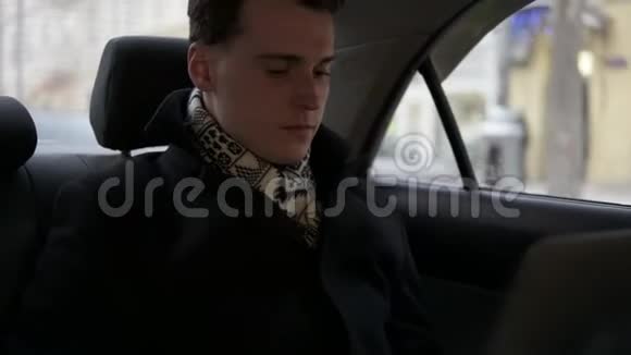 迷人的年轻男性骑在一辆车上笔记本电脑在他的腿上打开视频的预览图