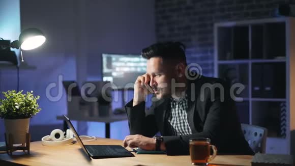 开朗的上班族在黑暗的办公室里与笔记本电脑聊天视频的预览图