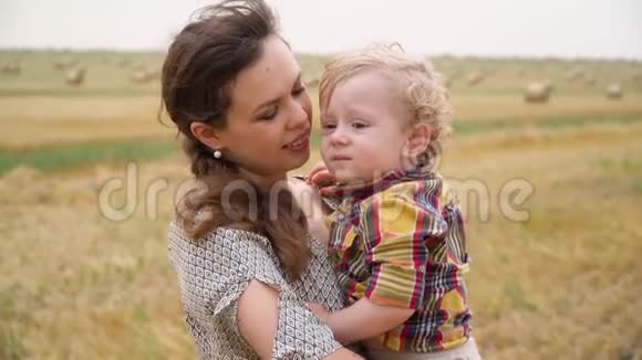 一位美丽的年轻女子她的怀里抱着一个金发小儿子在一片麦田里夏天带着包视频的预览图