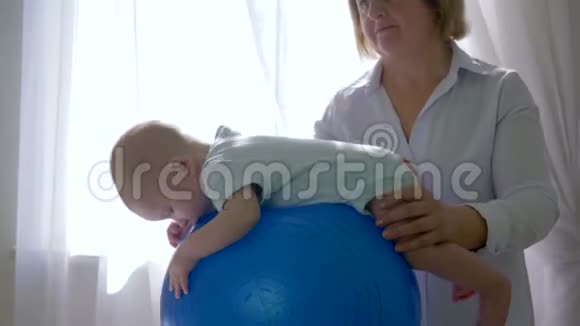 物理治疗师训练男婴在靠近窗户的大蓝球房间特写视频的预览图