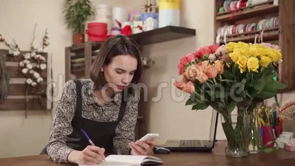 年轻女子在一家花店做花店工作她接受花束订单视频的预览图