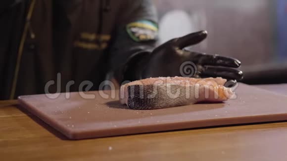 厨师用手把大片三文鱼和糖浆一起倒入穿黑色长袍和橡胶手套的人做菜准备视频的预览图