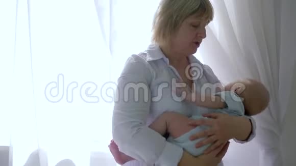 祖母在房间背光的窗户背景上抱着婴儿视频的预览图