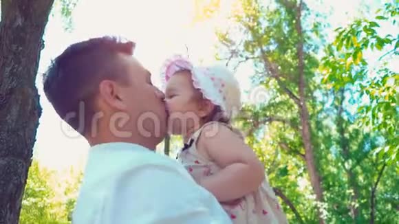 一位年轻的父亲把一个小女儿抱在怀里在绿树的背景下亲吻她视频的预览图