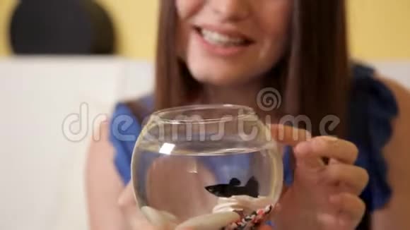 一个穿着蓝色西装的年轻微笑女孩坐在沙发上敲着一个小水族馆里面有鱼和手表视频的预览图
