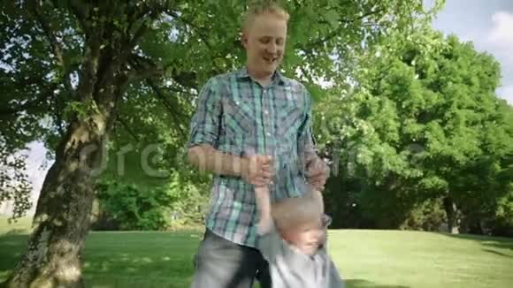 一个小男孩在公园里和他爸爸玩耍时的肖像爸爸摆动他的小男孩慢速高清视频的预览图