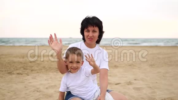 快乐的妈妈和宝宝坐在海边缓慢地挥动着微笑视频的预览图