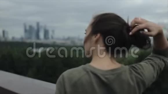 一个美丽的女孩看着城市的后景城市景观女孩让她的棕色长发垂下来视频的预览图