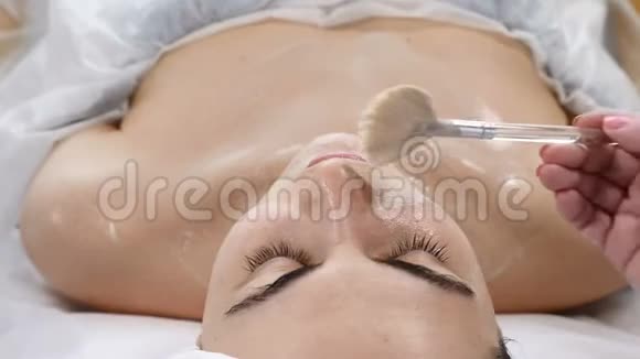 美容院年轻女子进行面部抗衰老手术美容师在女性面部及颈部涂抹液体面膜视频的预览图