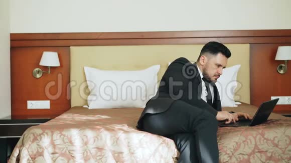 潘拍摄的集中商人西装工作在笔记本电脑而坐在床上在酒店房间商务旅行和视频的预览图