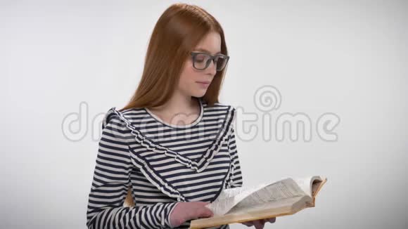 年轻甜美冷静的戴着眼镜的姜姑娘正在看书看着镜头白色背景视频的预览图