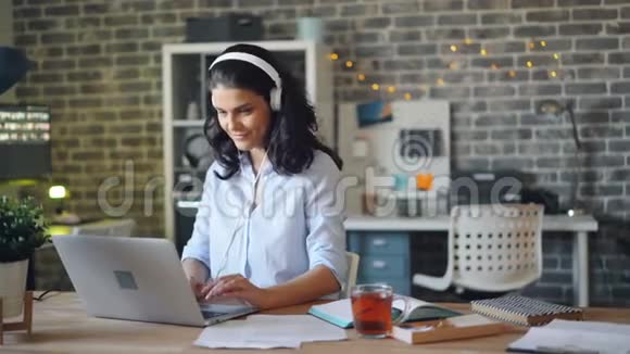 快乐的女孩用手提电脑打字用耳机听音乐视频的预览图