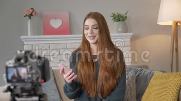 年轻的红发女孩博客作者微笑着在镜头上交谈用智能手机手势用手在家舒适视频的预览图