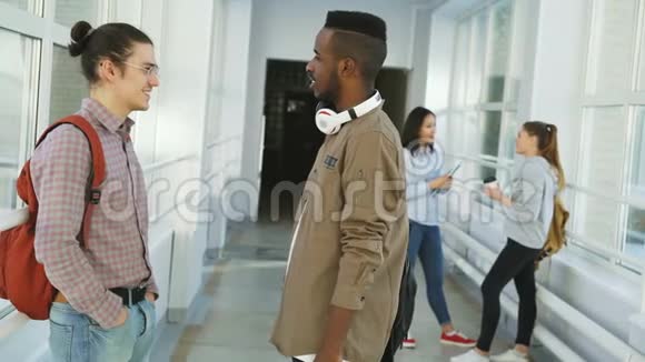 白人和非裔美国男学生站在大学大厅里聊天两个女孩在附近聊天视频的预览图