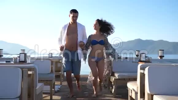 浪漫之旅欢乐的一对夫妇一起在码头上与美丽的海洋景观赛跑视频的预览图