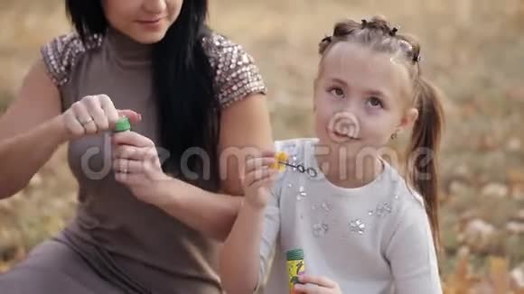 一对幸福的母女正在吹肥皂泡在温暖的秋天一家人在城市公园野餐视频的预览图