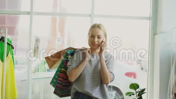 漂亮的金发女人在大商店的货架和栏杆之间走来走去用手机说话她带着视频的预览图