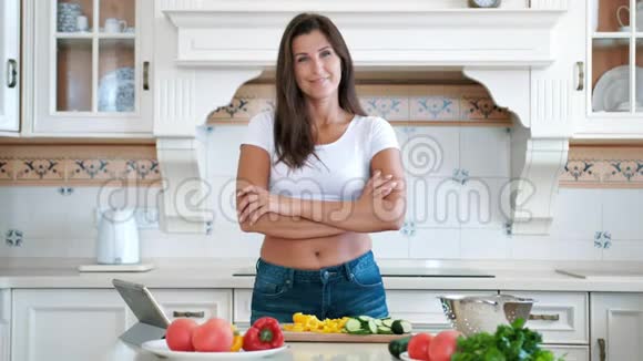 中长镜头微笑的女人用交叉的双手站在厨房做饭视频的预览图