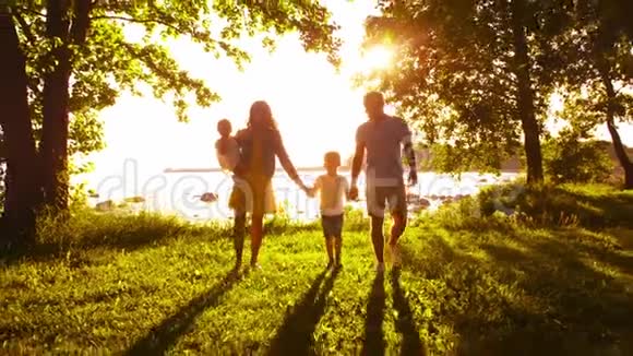 幸福的一家人走在海边农村的田野和树木日落或日出的暖色有爱心的父母视频的预览图
