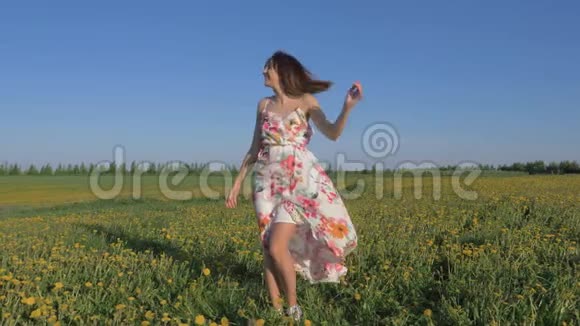 一个微笑的女人站在一个盛开的黄色田野里穿着一件连衣裙的肖像视频的预览图