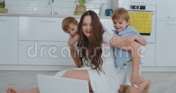 现代技术现代公寓爱妈妈和两个小儿子坐在客厅的地板上看着视频的预览图