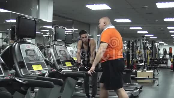 胖子和他的教练在跑步机上行走视频的预览图
