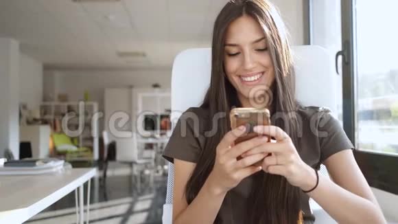 微笑着年轻的商务女性坐在办公室里用手机发送信息视频的预览图