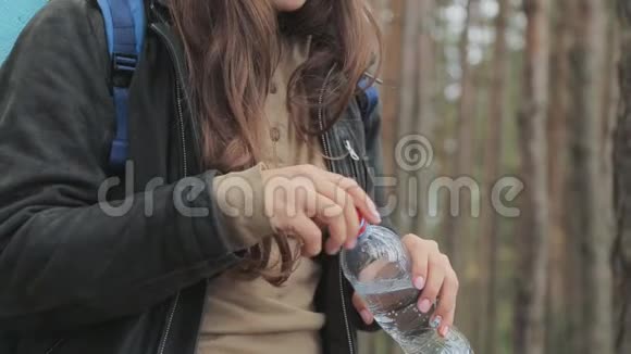 年轻的女旅行者站在森林里从瓶子里喝水自然纯水概念慢动作视频的预览图