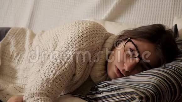一个年轻的女孩在一个冬天的晚上穿着白色毛衣坐在沙发上戴着眼镜看电视睡着了视频的预览图
