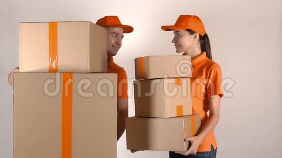 男女快递员穿着橙色制服运送多个纸箱浅灰色背景4K摄影棚拍摄视频的预览图