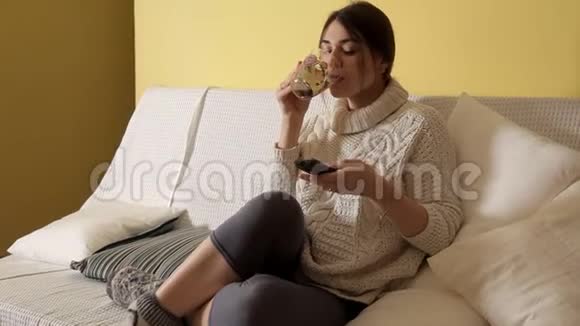 冬天晚上穿着舒适温暖毛衣的小女孩在家喝茶看电视视频的预览图