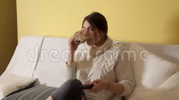 冬天晚上穿着舒适温暖毛衣的小女孩在家喝茶看电视视频的预览图