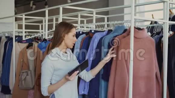年轻的女商人正在她的商店里检查衣服手里拿着平板电脑她的雇员过来询问视频的预览图