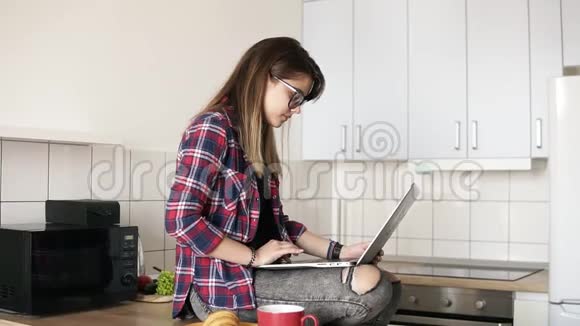 几个年轻快乐的嬉皮士在厨房接吻20的白人女孩坐在桌面上用笔记本电脑视频的预览图